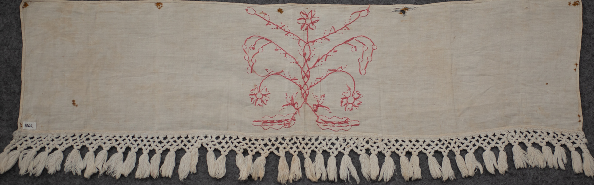 Hängkläde, del av. En liten bit av ett broderat hängkläde med hallandssöm. Bottentyg i tuskaftat vitt linne med ljusrött (rosa) broderi. Påsydd vit frans av bomull med omknutna tofsar i nederkanten. Längd= 100 cm. Bredd= 23,5 cm. Längd (frans)= 8,5 cm.