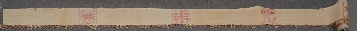 Hängkläde av halvlinne med bomullsgarn till korsstyngnbroderierna. Vit botten, broderier i rött. Knuten frans i rött. Längd 589 cm. Bredd 27 cm. Frans 8 cm. Märkt "1850", "O L N D". Frans: 70 mm.