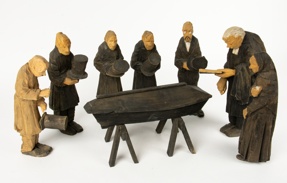Skulpturgrupp "Begravningen", bestående av 8 objekt föreställande 6 män en präst, en kvinna samt en kista på bockar. 
Gruppens figurer: 
1. Dödgrävare Hultgren i rock och med hatt i handen. H 256 mm.
2. Svartklädd bärare som håller en hatt. H 234 mm. 
3. Svartklädd bärare som håller en hatt. H 240 mm. 
4. Svartklädd bärare som håller en hatt. H 140 mm. 
5. Klockare Sjöström som håller en hatt. H 265 mm.
6. Prosten Arbman med mantelsläpet runt ena armen. I vänstra hande håller han en uppslagen bibel och i den andra skall han hålla en skopa (vilken saknas). H 272 mm.
7. Den sörjande änka i svart klänning och schal och vit näsduk. H 238 mm.
8. En kista på två bockar, L 290 mm.