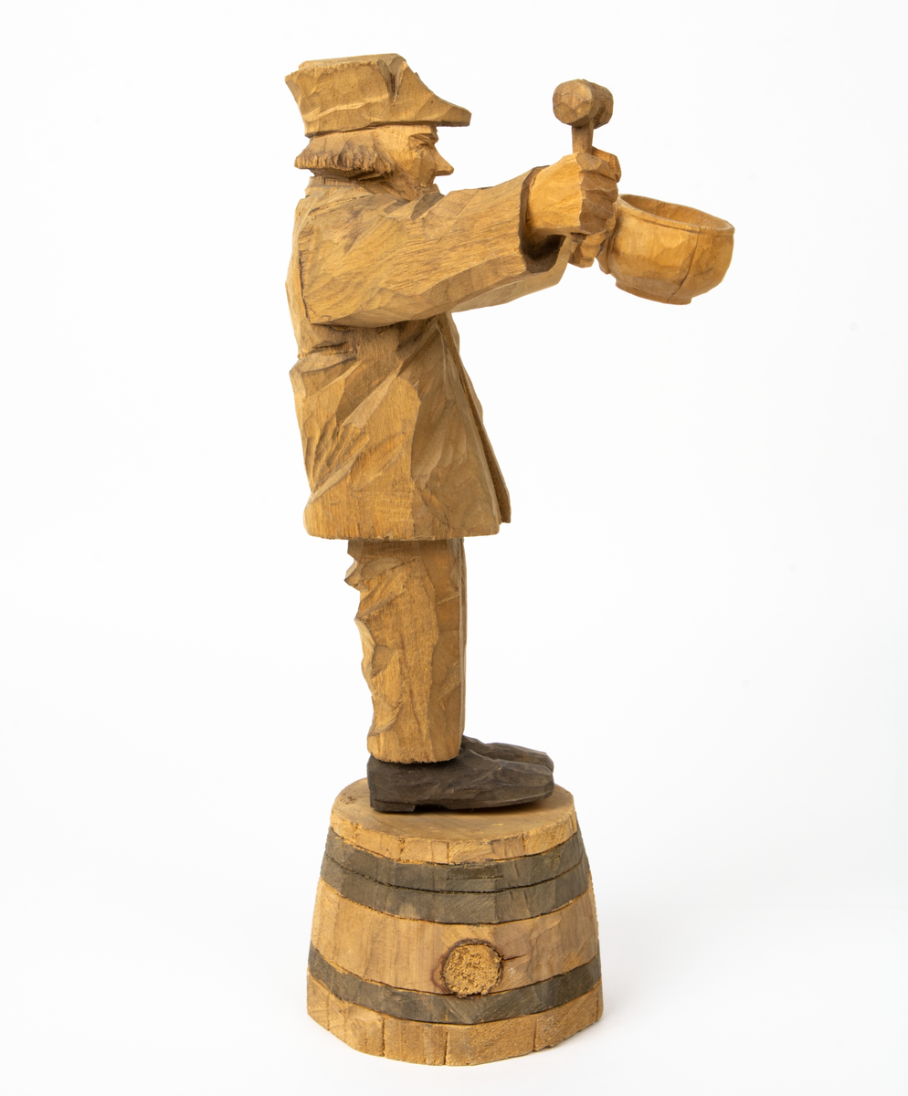 Auktion, skulpturgrupp föreställande sex personer som lyssnar till en auktionist. 
Figurer:
1. Man med händerna i fickorna, randig rock och rutiga byxor, pälsmössa. H 282 mm. 
2. Man med rock och pälsmössa. H 283 mm. 
3. Man med hatt och rock. I handen håller han ett par stövlar, H 274 mm. 
4. Kvinna insvept i schal. Hon håller ett klädesplagg, l 268 mm. 
5. Kvinna med schal och lång kjol. Hon håller ett klädesplagg, H 264 mm.
6. Kvinna insvept i schal.
7. Auktionist, "Ropar-Olle", som håller upp en potta. Den andra handen håller en klubba. Han står på en upp och nedvänd tunna.
