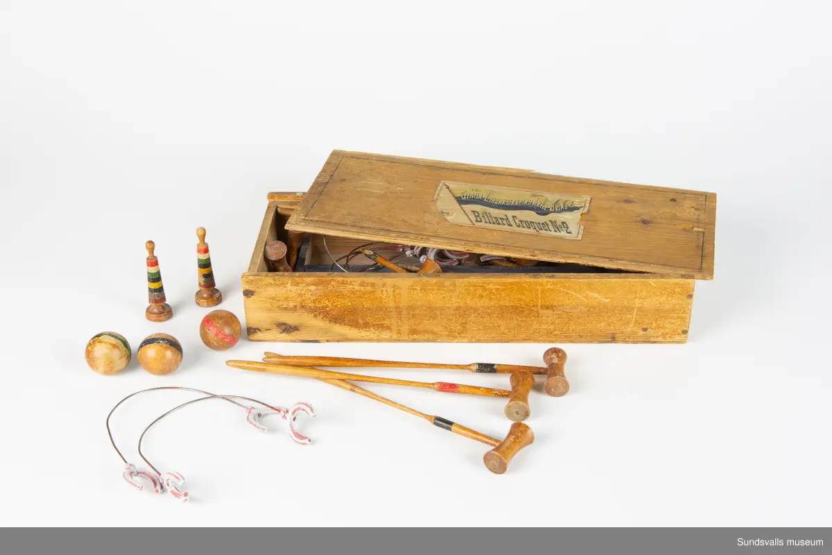 Billiardcroquetspel bestående av: Tio stycken bågar med gjutna hästskoformade stöd. Åtta stycken träklot, åtta stycken klubbor, samt två stycken målpinnar. Klubbornas längd är 25,5 cm. Spelet ligger förvarat i en skjutask med etikett på locket 'Från Gemla Leksaksfabrik Aktie Bolag Billiard Croquet No 2'.