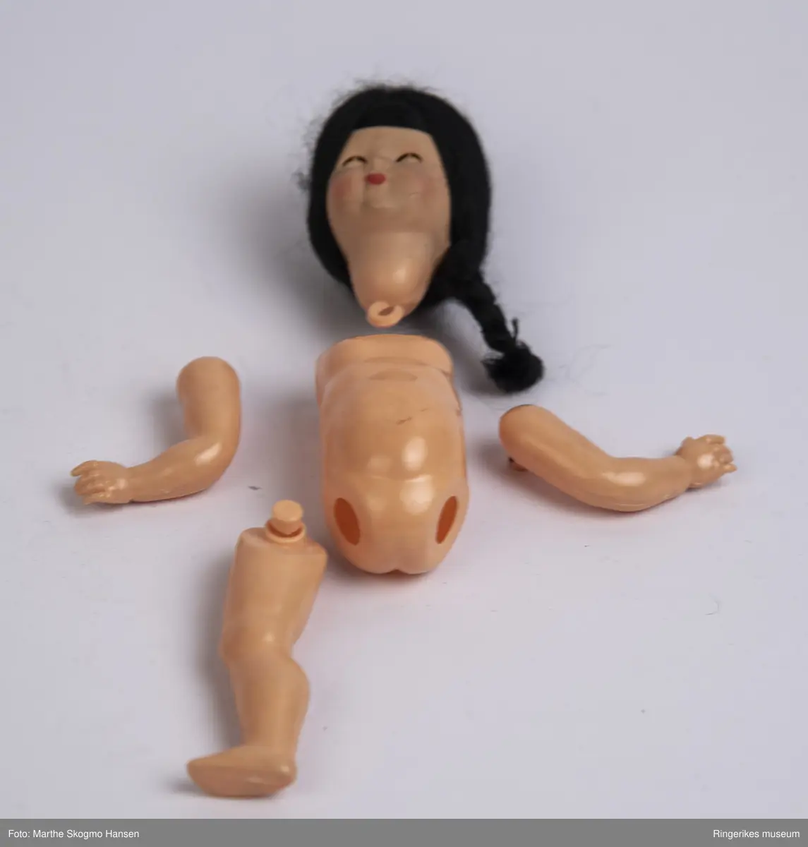 Dokke med blå soveøyne og svart hår som er samlet i en flette på siden av hodet. Munnen er rødmalt. Ben, armer og hode har vært holdt fast til kroppen med strikker, men disse har nå forvitret, så alle delen er løse. Originale klær og sovepose fulgte med. Dokka har en logo stemplet inn på ryggen, og påskriften "Made in Italy".