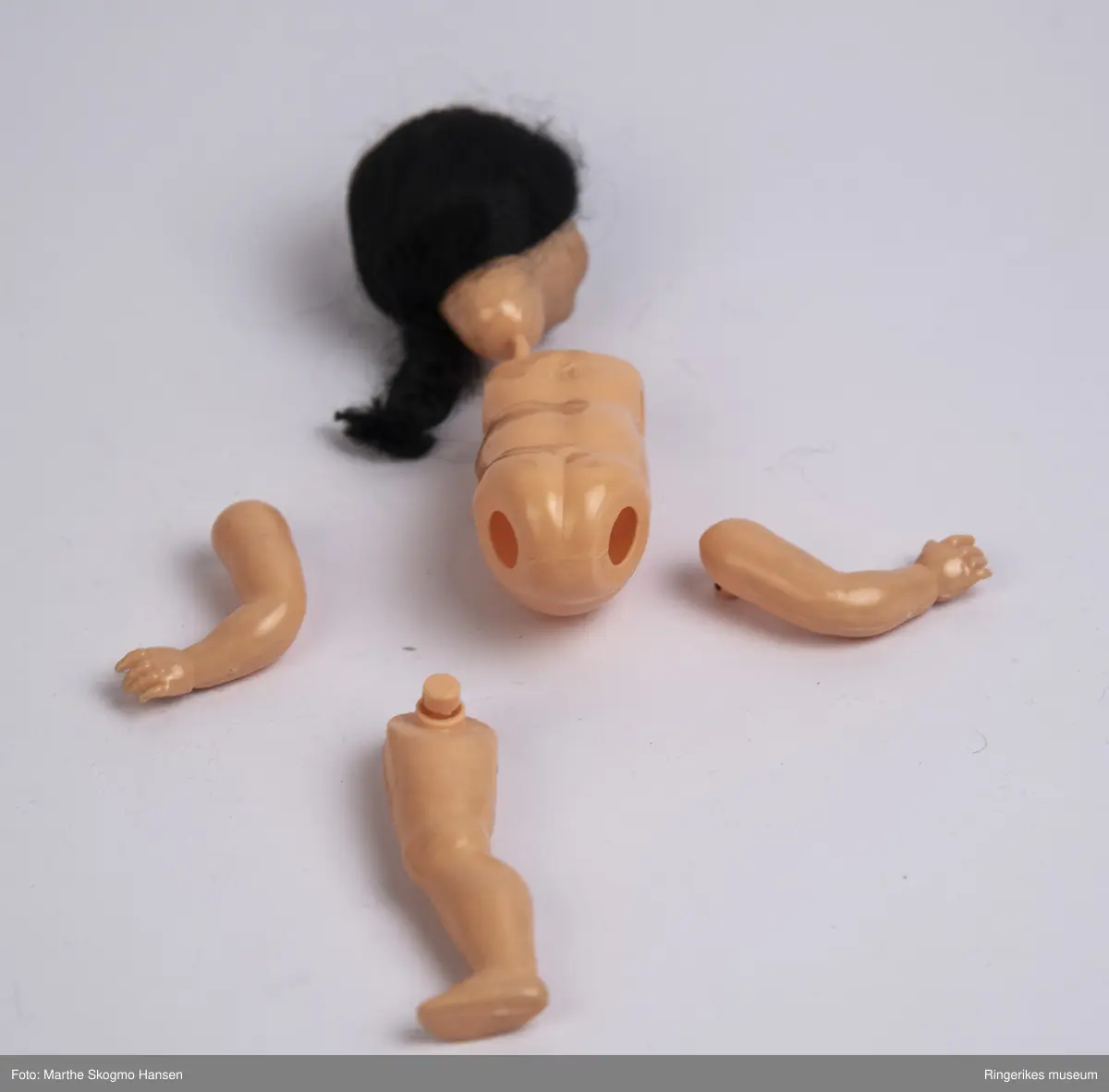 Dokke med blå soveøyne og svart hår som er samlet i en flette på siden av hodet. Munnen er rødmalt. Ben, armer og hode har vært holdt fast til kroppen med strikker, men disse har nå forvitret, så alle delen er løse. Originale klær og sovepose fulgte med. Dokka har en logo stemplet inn på ryggen, og påskriften "Made in Italy".