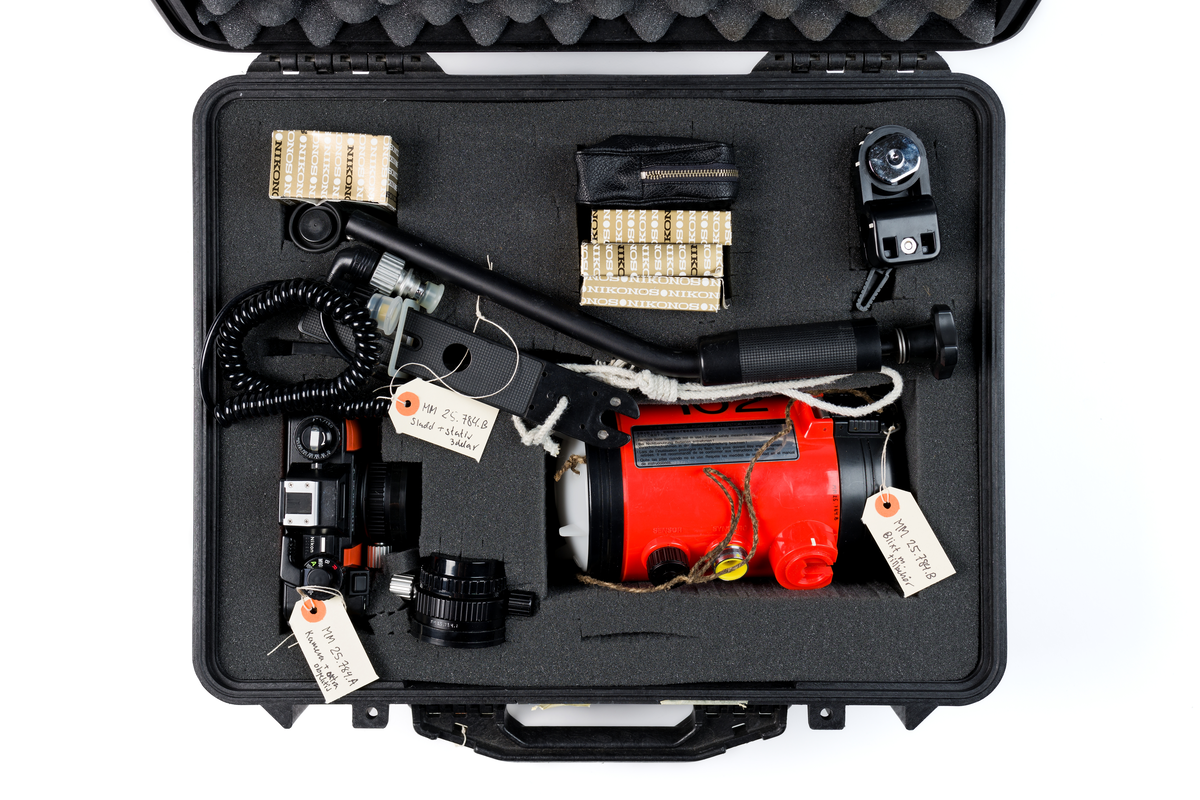 Undervattenskamera Nikonos V. Svart kamera med detaljer i orange. Extra objektiv bredvid. Kameran märkt i vitt: "Nikonos-V"