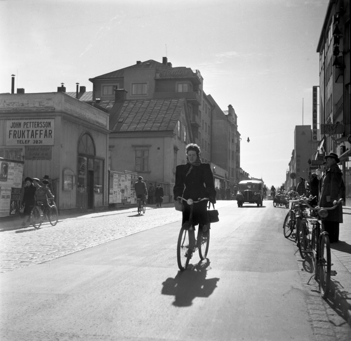 Mycket har förändrats i gatubilden sedan fotografen fångade ögonblicket utmed Sankt Larsgatan i Linköping. Bilden kan dateras till våren 1949 och inom kort ska husraden närmast till vänster rivas för att ge plats för nya hus och ny gata i Göran Dyks. I handelsboden från ett äldre Linköping drev dock John Petterssons sin fruktaffär ännu en tid. Adressen skulle idag motsvara Sankt Larsgatan 25.