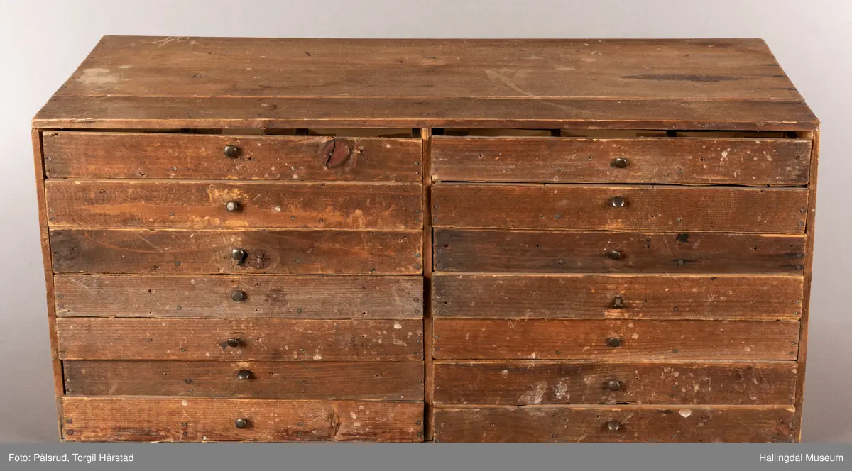 En liten skuffeseksjon i brunt tre med 17 skuffer i to rader. Hver skuff er oppdelt til å oppbevare bunker med frimerker, og har en liten sort metallknatt midt på framsiden av hver skuff som fungerer som håndtak. 