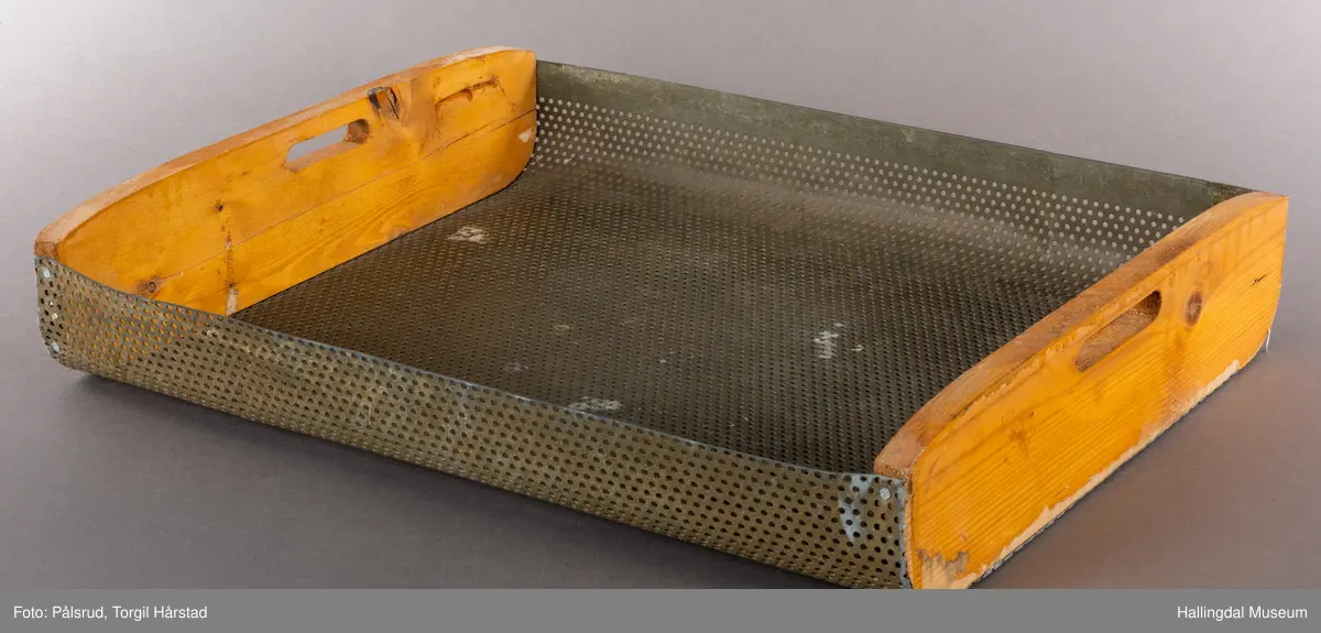 Et rektangulært vaskebrett med to treender med hull til håndtak i hver endte og en bøyd metalldel med hull i for at vann skal renne av.