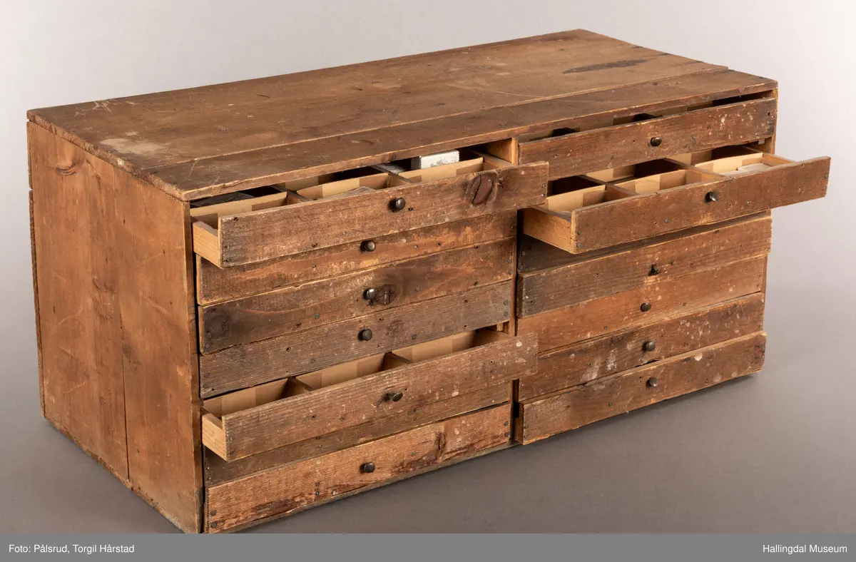 En liten skuffeseksjon i brunt tre med 17 skuffer i to rader. Hver skuff er oppdelt til å oppbevare bunker med frimerker, og har en liten sort metallknatt midt på framsiden av hver skuff som fungerer som håndtak. 