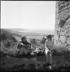 En man och en kvinna sitter på en mur vid Brahehus slottsruin, utsikt mot Gränna.