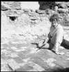 En kvinnlig arkeolog sitter på stengolvet i Brahehus slottsruin.