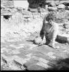 En kvinnlig arkeolog sitter på stengolvet i Brahehus slottsruin.