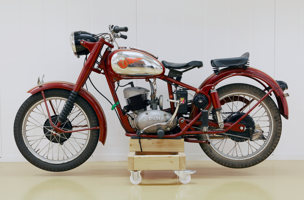 Motorcykel, modell NV 35, 250 kubik, årsmodell 1952. DKV-motor på 11,5 hästkrafter, tre växlar. Mörkt rödlackerad med guldränder på stänkskärmarna. Förnicklade detaljer. Bensintanken rödlackerad med förnicklat parti på båda sidorna med vingmärke i rött och guld med riksäpple och bokstäverna NV. På motorn i relief: DKW. På bensintankens förnicklade lock text: Använd Mobiloil från Vakuum Oil Company. Batteri NOAK svart gult och rött. Generator märkt HELLA, Germany. Svartlackerad stor lykta fram med hastighetsmätare, svartlackerad baklykta. Svart stor gummisadel, sits bakom av svart läder. Svarta gummihandtag på styret och svarta gummipedaler.  Svarta däck med svarta nav. Förnicklad cykelpump. Rödlackerat stöd.  Hållare för registreringskyltar.
