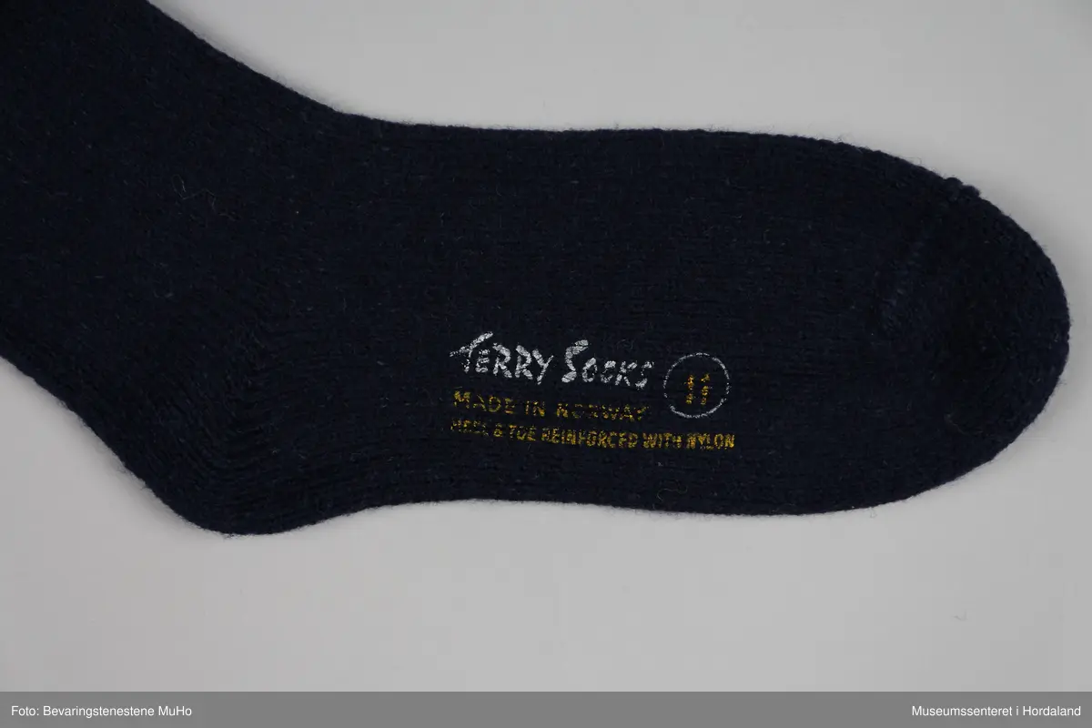 Eit par marineblå strikka ullsokkar frå Samnanger fabrikker i str. 11. Den eine sokken har tekst trykt på under foten: "Terry socks, made in Norway, reinforced with nylon, 11". sokkane har vore festa saman med ein papimerkelapp med ein skiløpar på, og teksten "Safa sport - sterk og varm".