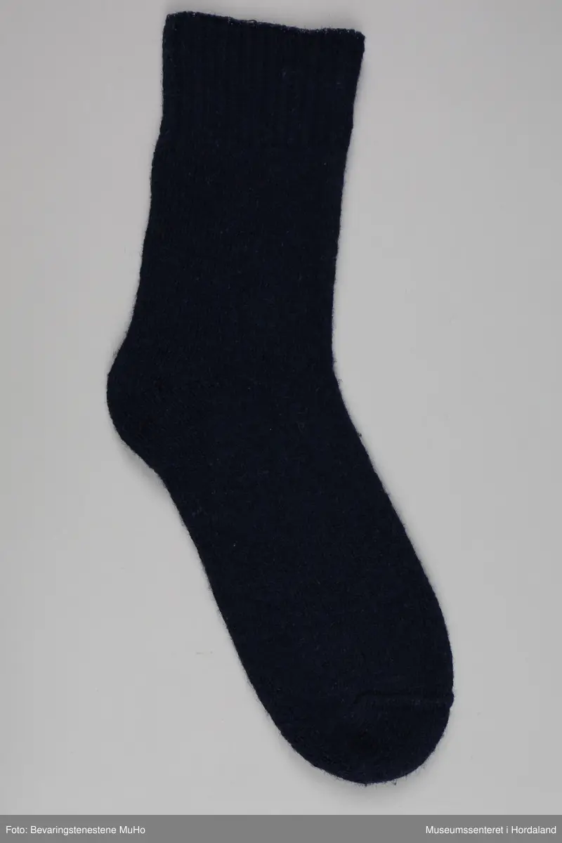 Eit par marineblå strikka ullsokkar frå Samnanger fabrikker i str. 11. Den eine sokken har tekst trykt på under foten: "Terry socks, made in Norway, reinforced with nylon, 11". sokkane har vore festa saman med ein papimerkelapp med ein skiløpar på, og teksten "Safa sport - sterk og varm".
