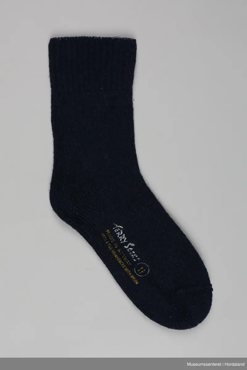 Eit par marineblå strikka ullsokkar frå Samnanger fabrikker i str. 11. Den eine sokken har tekst trykt på under foten: "Terry socks, made in Norway, reinforced with nylon, 11". sokkane har vore festa saman med ein papimerkelapp med ein skiløpar på, og teksten "Safa sport - sterk og varm".