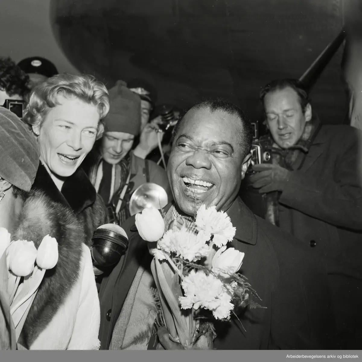 Louis Armstrong ankommer Oslo via Fornebu flyplass 2 februar 1959. Fra venstre: Lucille Wilson (hans kone), nrk-reporter Unni Børde og Louis Armstrong..