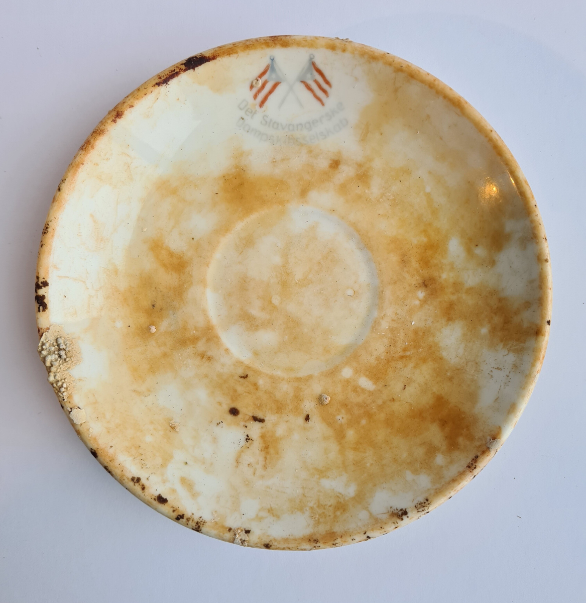 Kaffeskål av hvitt porselen merket "Det Stavangerske Dampskibsselskab" med to rederiflagg.

