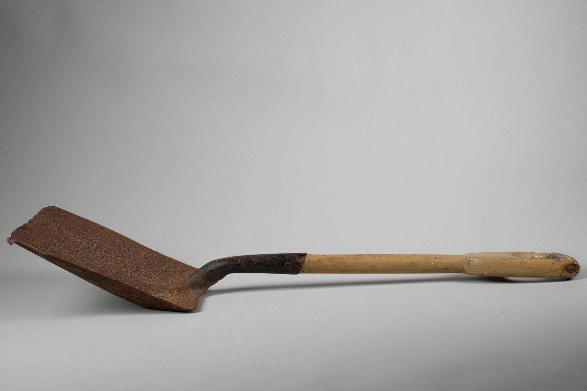 Firkantet fyrbøterspade i jern med malt grønn/brunfarget treskaft .
Jernet er rustent.
Merke øverst på treskaft både på for og bakside