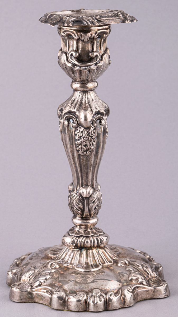 Ljusstake, silver, fotens kant något uddig. Fonden med tre rocailler samt växtornament. Ljuspipan blomprydd.
Ingår i ett par.

Ljuspipa, stämplad med bl.a. kattfot och GM.
Tillverkad Stockholm, Gustaf Möllenborg,
stake 1865, ljuspippa 1863.
Stil: Nyrokoko.