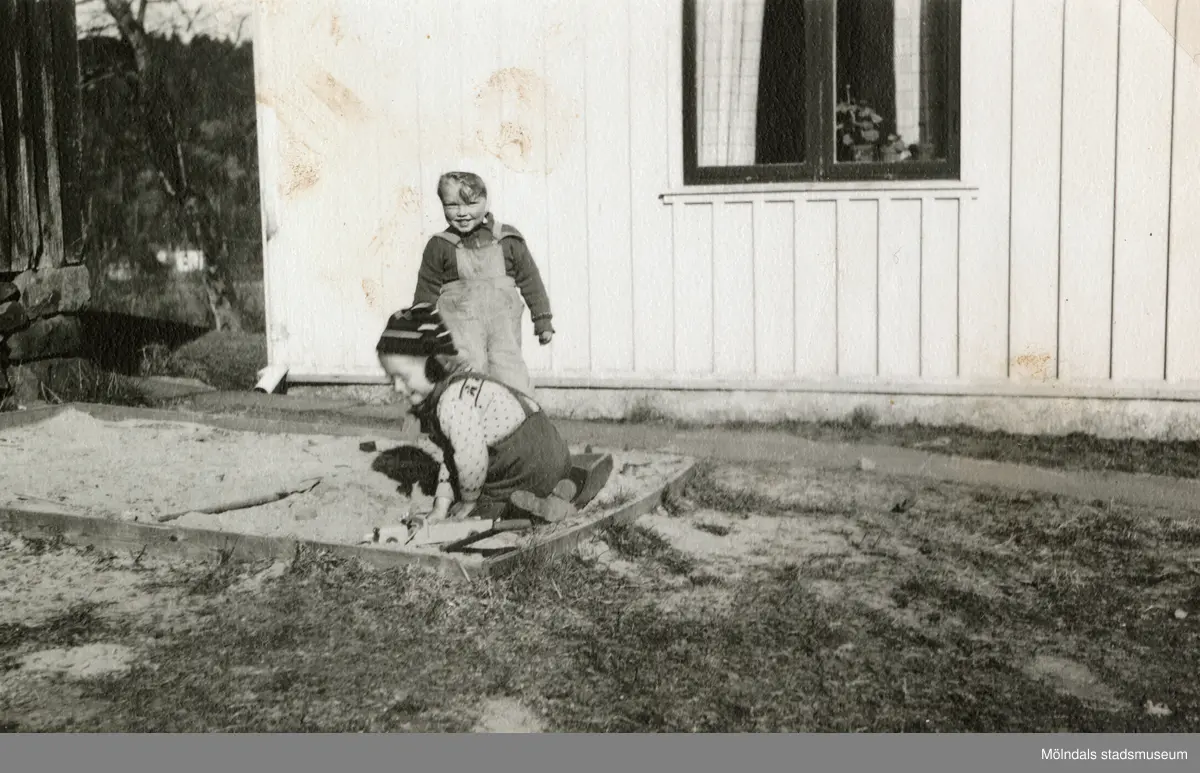 Kjell Johansson (född 1945) och Eva Pettersson (född 1944, gift Kempe) leker i sandlådan vid Torrekulla gård 1947. På bottenvåningen bodde familjen Johansson, familjen Pettersson hyrde på andra våningen.