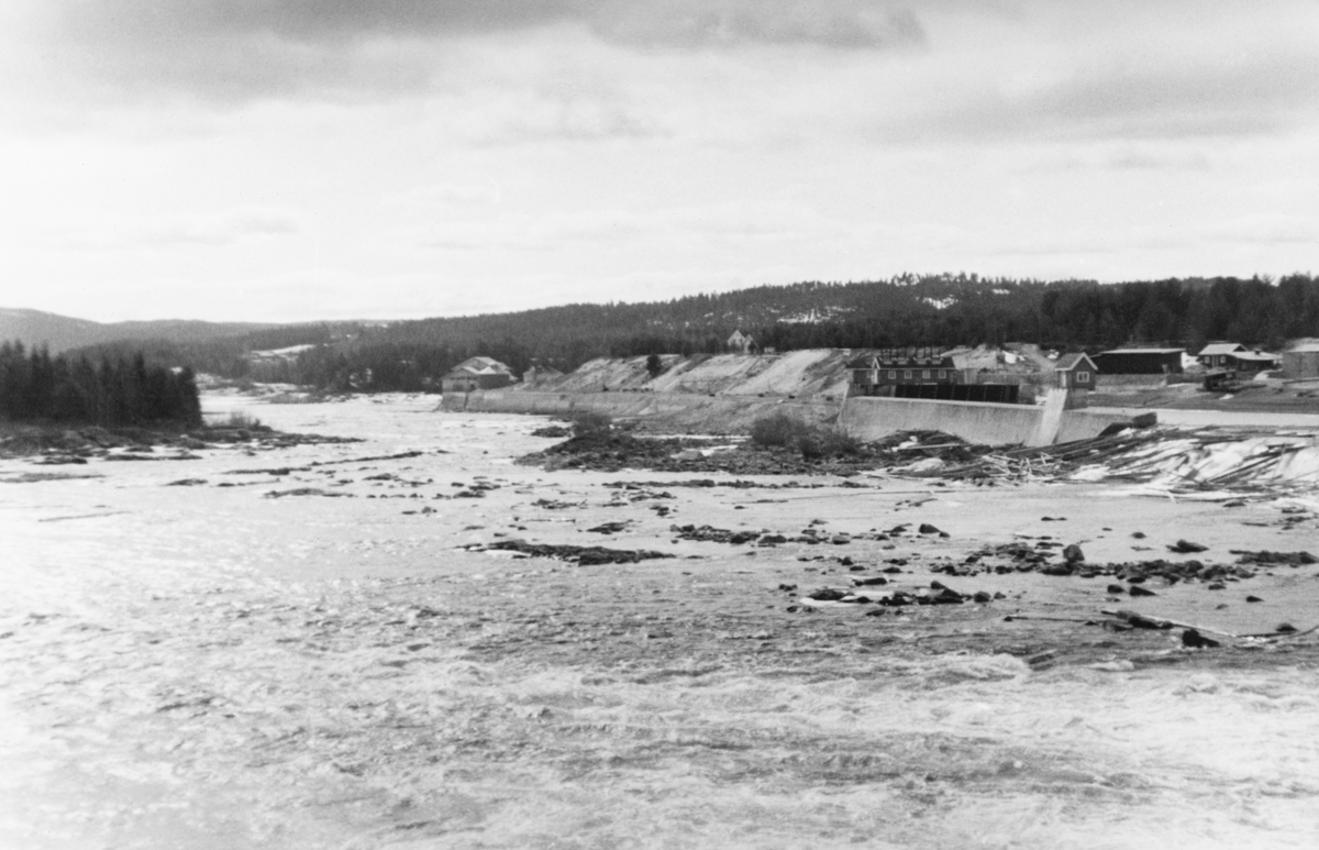 Skjefstadfossen i Heradsbygda i Elverum, fotografert i april 1938.  Fotografiet er tatt fra østsida av fossen, omtrent ved dammen.  I forgrunnen ser vi kvitskummende Glomma-vann, som nettopp har passert dammens 312 meter lange overløp.  På motsatt side av elva, til høyre i bildeflata, ser vi inntaksdammen for turbinvann med lukehus på damkrona. Derfra gikk det to grove, betongstøpte rør ned til kraftstasjonen, drøyt 400 meter lengre nede. Turbinrørene var nedgravd langs elvebredden, noe skulle begrense faren for isdannelser i kuldeperiodene vinterstid.