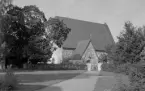 Torsångs kyrka. Den skuggade kanten under taket är rött tegel. Framkanten på portalen samt teglet intill är rött. Taket har svartblå skifter. Kyrkans ingång som delvis skymmes av pelaren är av rött tegel. Även inramningen till fönstret är rött tegel. Läs mer om Torsångs kyrka i boken. Dalarnas kyrkor i ord och bild.