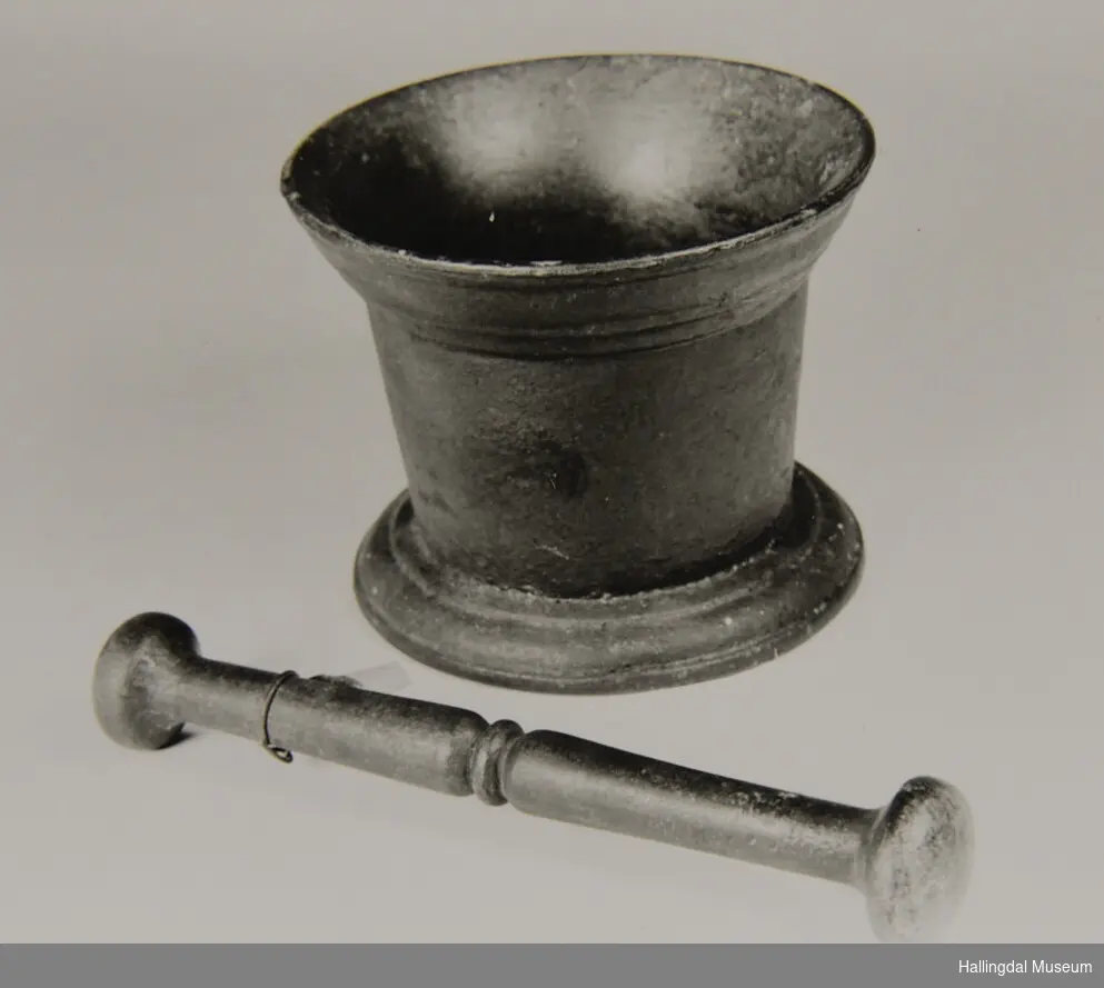 Mortar med innoverskrånande fot. Deretter lett utoverskrånande veggar. Mortaren har sirkulært tverrsnitt.
Knusaren har sirkulært tverrsnitt. Ei kule i kvar ende, ein ring på midten.