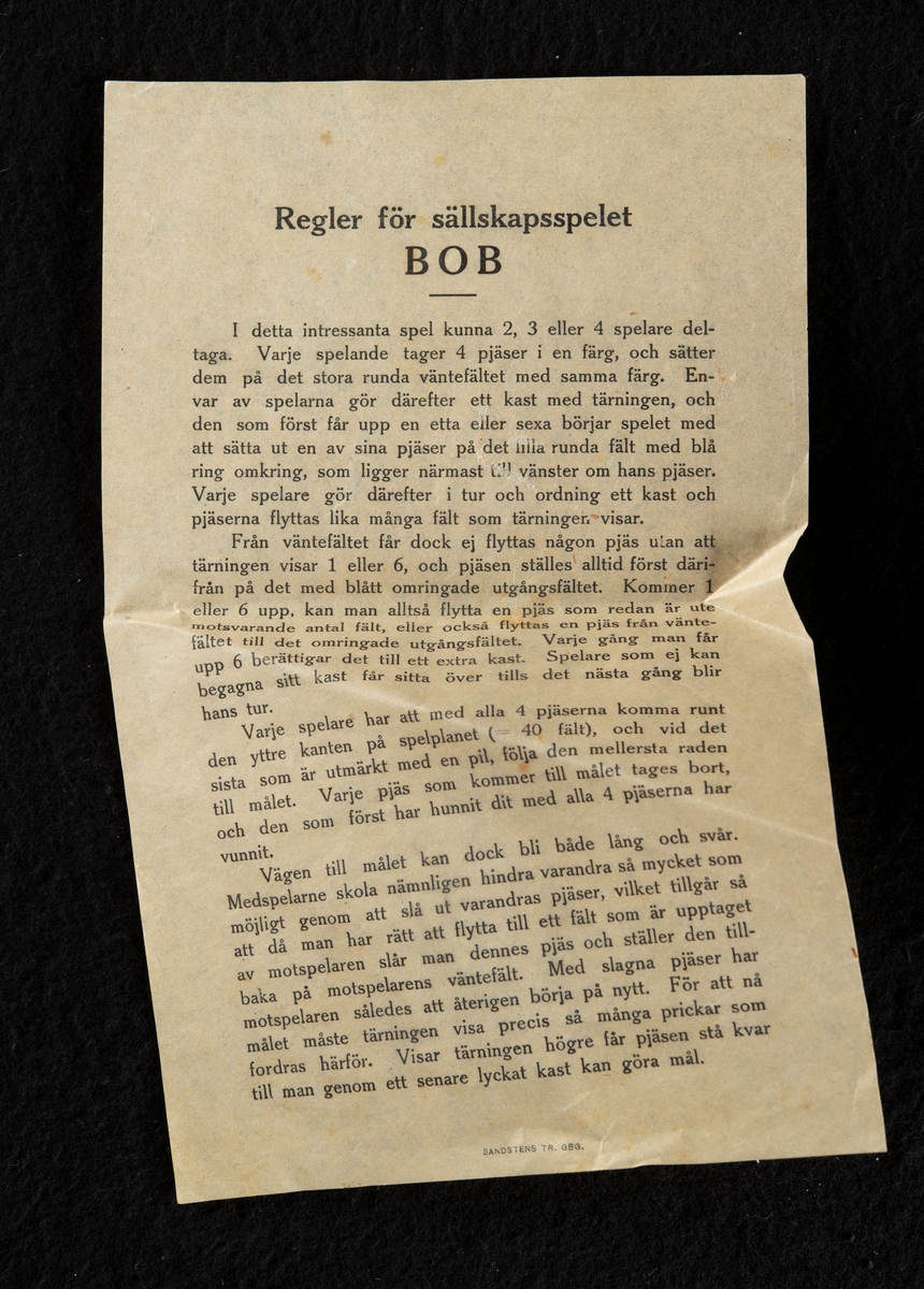 Spel i originalförpackning av papp, med spelplan, instruktioner, tärning och spelpjäser. En spelpjäs saknas. Förpackningen är en kvadratisk, platt ask i ljusgrön, bleknad färg med text på framsidan. Spelplanen är formad som ett kors, bestående av tre rader med prickar för spelpjäsernas placering, i fyra olika färger. I varsitt hörn är spelarnas "bo" markerat, där deltagarna startar, vart och ett i varsin färg; rött, blått, gult och grönt.