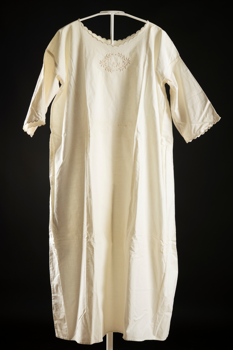 Nattlinne av vitt vävt tyg. Halvlång ärm med broderad kant. Monogram "EN" med krans av blad runt broderat på bröstet. Broderi kring halslinning.
