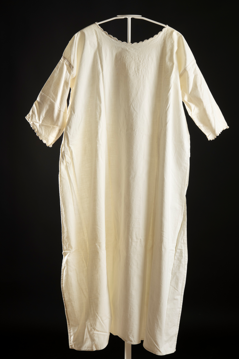 Nattlinne av vitt vävt tyg. Halvlång ärm med broderad kant. Monogram "EN" med krans av blad runt broderat på bröstet. Broderi kring halslinning.