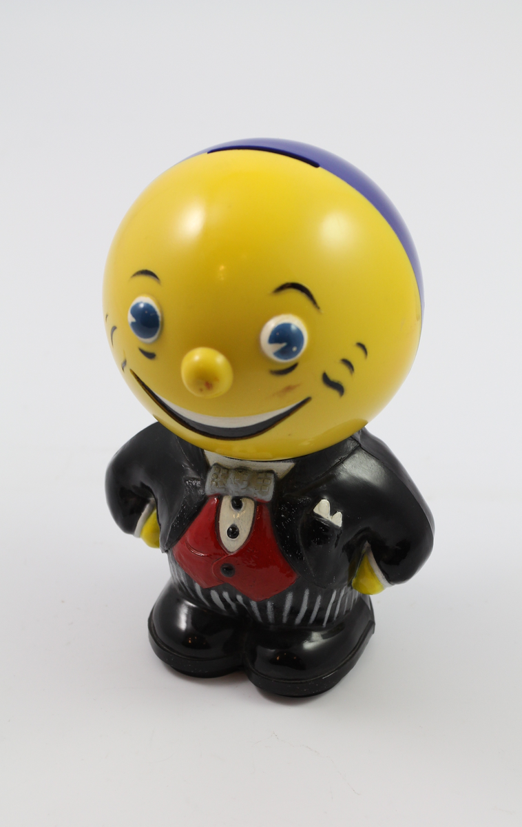 Sparebøsser i form av to plast figurerer og en glassbeholder. En kenguru med blått skjerf og hvitt hår, en dresskledt figur med gule hender, gult stort rundt hode og blått bakhode, en rektangulær glassbeholder med skrånede hjørner og metallokk.