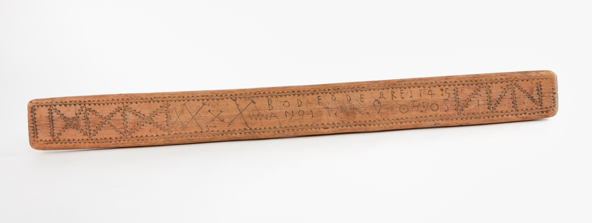 Födelsesticka i form av avlång bräda. Skuren dekor på ovansidan med bl.a. fyra korslagda pilar, dalpilar? Skuren märkning på ovansidan: "BOD FÖDE ÅRE 1745",  "ANO 1749 OHEOS", "E".  Skuren märkning på undersidan "KOD". 
Ev. rester av spikhål i var kortände.