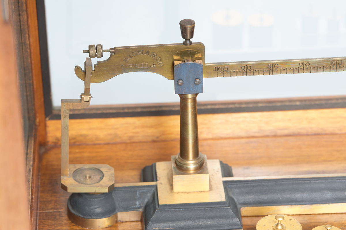 Spesialvekt, balansevekt a) og skap b). Vekten er av messing, og er gradert fra 0-100 gr. Skapet er av tre og glass med skuff for tilbehør. Antatt datering ca 1910, brukt ved Kapp Melkefabrikker og merket; Nestle No 168. Vekta er produsert av J. Richards Phil A/S.