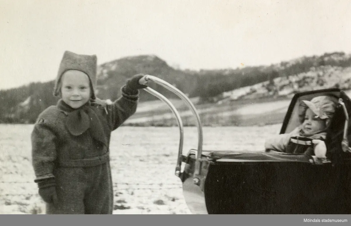 Eva Pettersson (född 1944, gift Kempe) kör kusinen Stina Krantz i barnvagn år 1946. Vommedal och Brattåsberget ses i bakgrundens mitt. Eva är dotter till Bror och Rosa Pettersson (född Krantz). Stina är dotter till Edit och Östen Krantz.