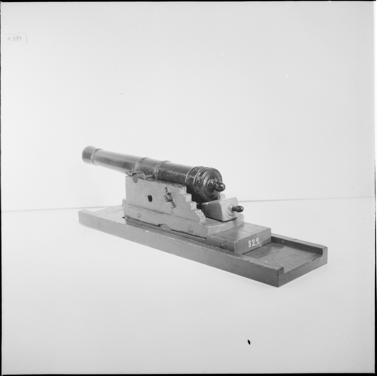 Kanonmodell: galérlåda med släde, beslagen, samt kanon. Lavetten av trä, rödmålad. Kanonen av järn, svartmålad. Tillbehör: 1 st ställhult. Lavetten L = 440 mm B = 110 mm H = 130 mm.