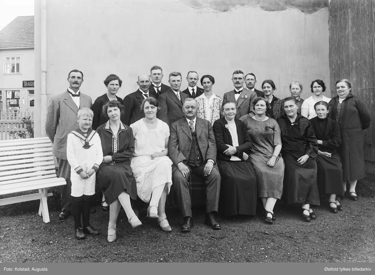 Gruppe fotografert utendørs, ukjent sted og ukjente personer.  I bakgrunnen skilt for barber og frisør.