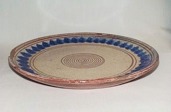 Gult fat av lergods dekorerad med blått mönster samt bruna ränder där leran är framskrapad. Brun undersida med glasering.