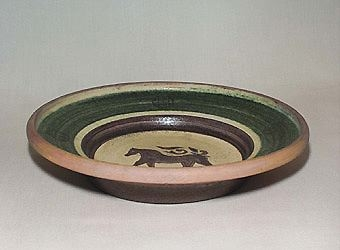 Brunt fat av lergods med grön kant på insida och i botten en häst inristad i den gula engoben. Undersida är ristad i vågmönster samt delvis glaserad i en mörkbrun färg och transparent glasyr.