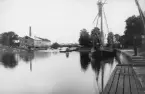 Vy över Nykvarns hamn 1901. Reservation ska emellertid tas för årtalet 1892 som förekommande datering. Industribyggnaden till vänster uppfördes 1874 och huserade  till en förödande eldsvåda 1913 en rad olika verksamheter. Bortom bron anas den dammanläggning som tillkom för att uppströms höja Stångåns vattenstånd och möjliggöra funktion av Nykvarns sluss till höger i bilden.