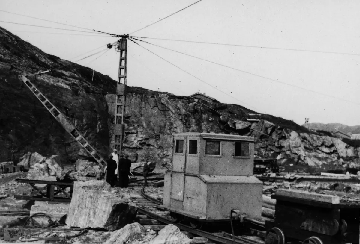 Fra steinbrotet i Ergan i Bud der det vart teke ut stein til andre byggetrinn av moloen. Moljå i Bud. Ferdig i 1951. Donigen på skinnegangen er eit lokomotiv og som gjekk med dieselmotor. Store steinblokker vart lagt på tralla til høgre ved hjelp av krana og tranportert utover den delen av moloen som var ferdig, og tippa utfor enden på moloen. Krana vart driven av dampmaskin. Det var også borane som laga hol for sprengstoffet som sprengte ut steinblokkene.