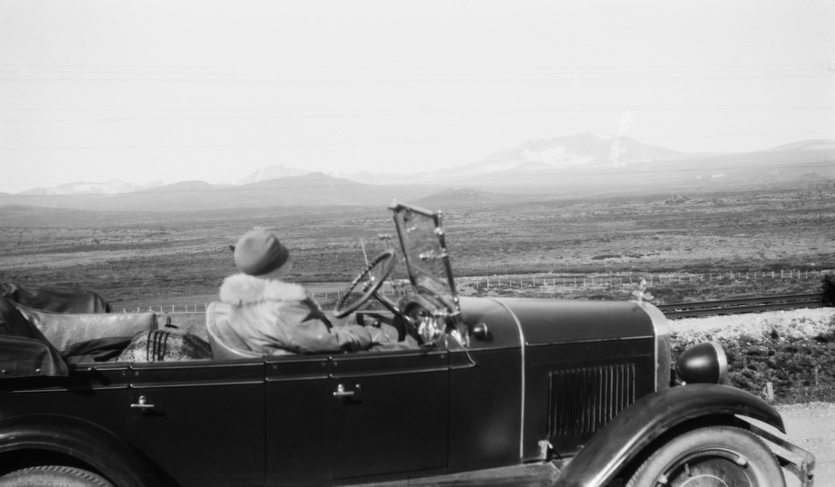 Stopp ved Hjerkinn på veg over Dovrefjell i åpen bil, type Chevrolet 1927-28-modell med jernbanesporet og Snøhetta i bakgrunnen