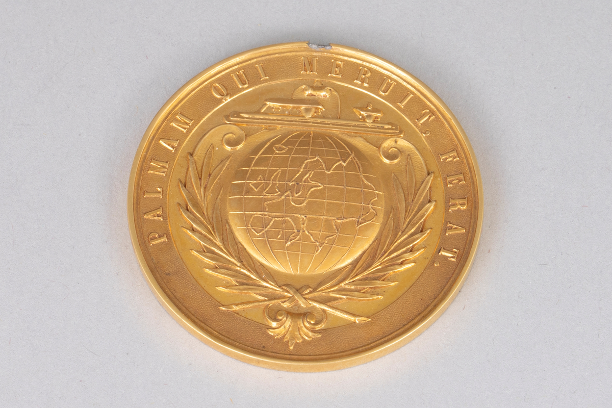Rund medalje i forgylt metall med opphøyet rand og punslet dekor. På avers er det en globus med palmegrener rundt og en skøyte over. Innskrift langs randen. På revers er det en laurbærkrans, dannet av to kryssende grener med sløyfe rundt, ellers glatt overflate. Langt gult og turkis ripsbånd festet til en ring som er brukket av medaljens kant.