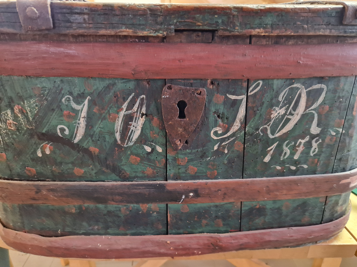 12 staver satt sammen med 3 treband, med bunn og lokk. 2 jernbeslag over lokket, og lås med nøkkel. Malt.