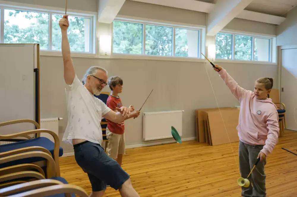 En mann sjonglerer med tau og plasttallerken. To barn står rundt og lærer