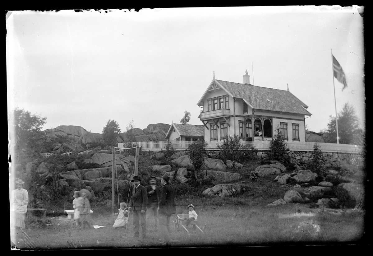 Voksne og barn i hage nedenfor ukjent hus