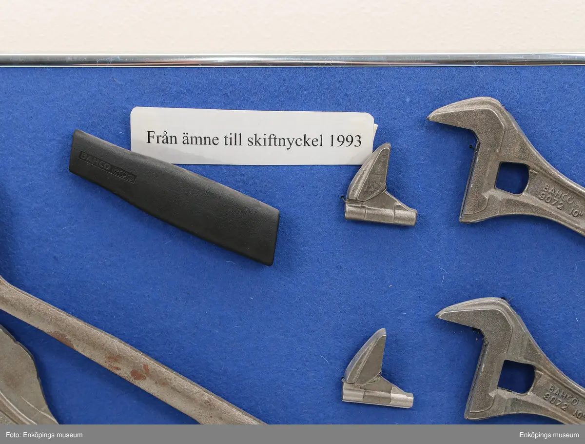Tavla med metallram, blå textil "Från ämne till skiftnyckel 1993".