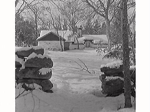 Minas stuga inbäddad i snö. Stugan var ursprungligen en linbasta men byggdes vid 1800-talets slut om till backstuga. Stugans sista invånare var Mina Johansson som dog 1942. Stugan köptes då av Knut Öberg, fotografen Runes far, som lät renovera stugan och sedan skänkte den till hembygdsföreningen.