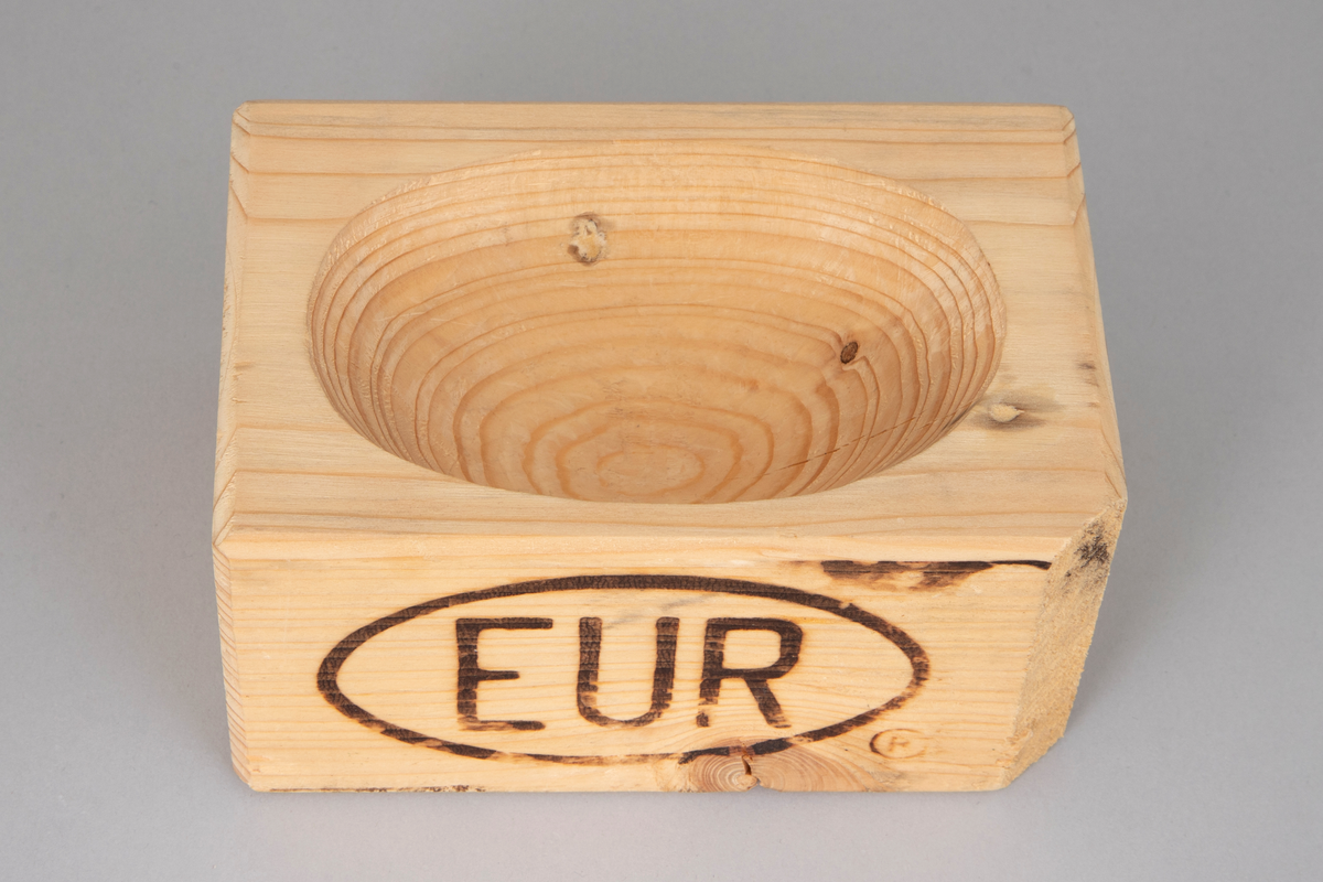 Skulpturell objekt i form av en rektangulær klosse med avrundede hjørner laget av europall. Bokstavene EUR med oval ring rundt er brent inn i den ene langsiden. Utskåret som til en bolle på oppsiden, med spor etter tappjern/treskjærerjern. Bollen er omtalt som et saltkar på plakaten NK2007-419-006.