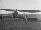 Militärt flygplan Albatros B.I tillhörande Österrike-Ungern står på en åker. Hjulen är nedsjukna i marken. En flygare och ett en pojke står vid planet.