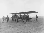 Militärt flygplan Fokker B.I märkt 03.28 står på ett flygfält. Militärer omkring flygplanet. Vy snett framifrån.